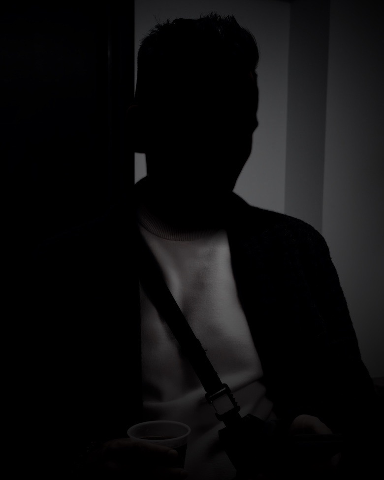 M, the photographer, face in shadow, holding a coffee and a phone